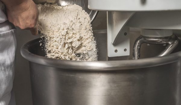Vertical photo of a person adding flour in an industrial mixer to make artisan bread